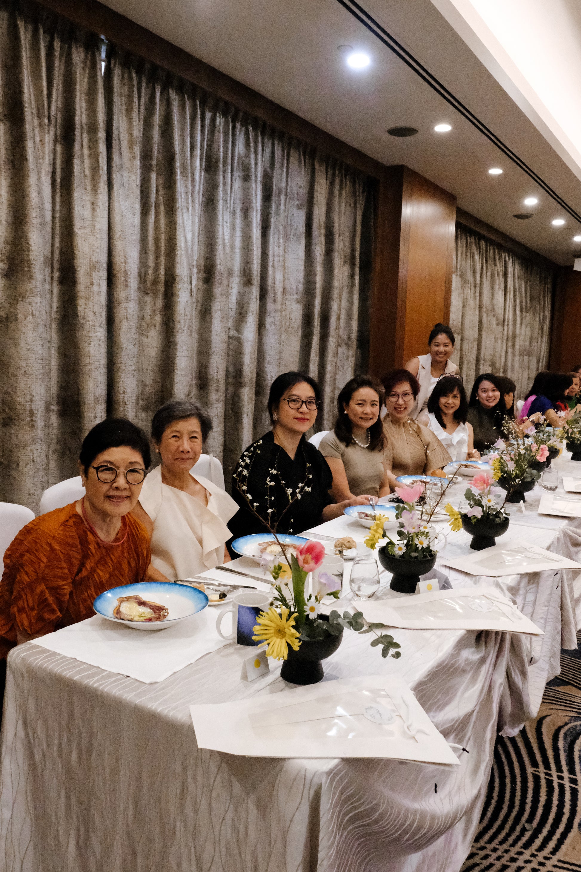 Group of women sitting at a formal event with floral centerpieces on tables.